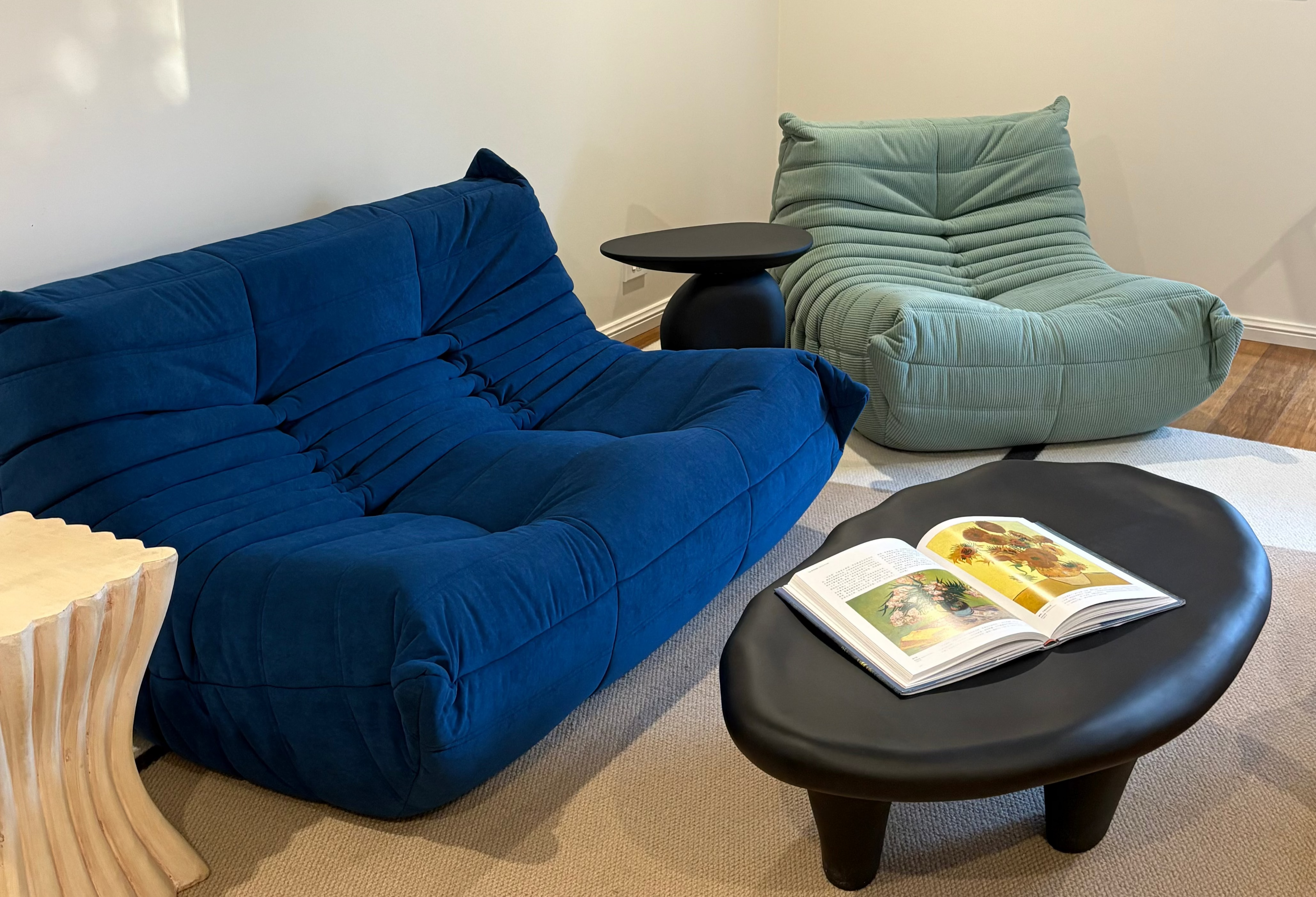 Modern living room with blue sofa, green chair, and round black coffee table.