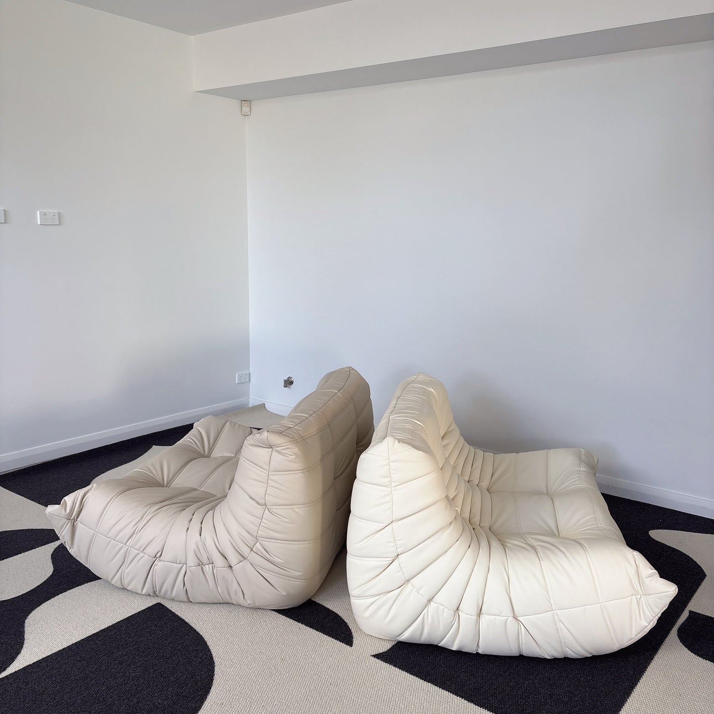 Two beige lounge chairs on a black and white patterned floor.