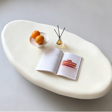 White oval table with a book, bowl of oranges, and diffuser on a light gray background