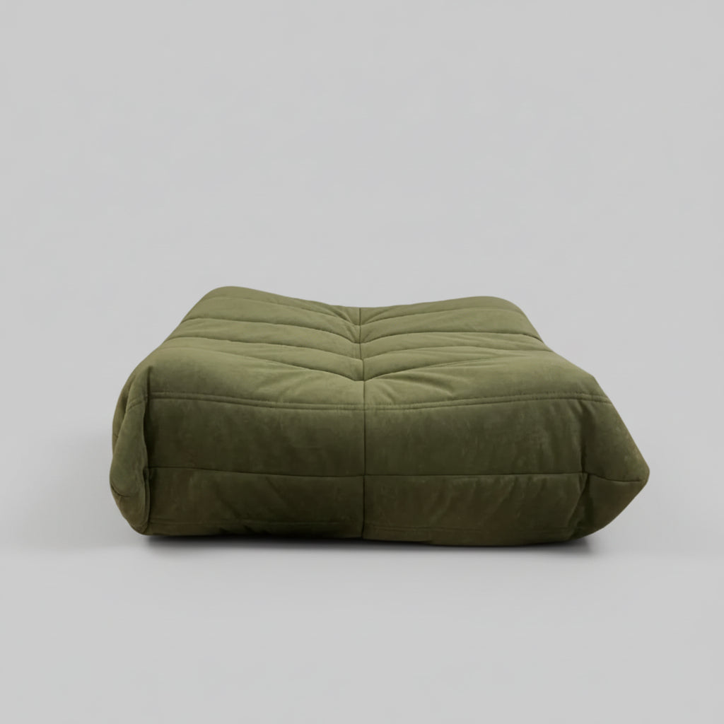 Green cushion on a wooden floor with a colorful abstract painting on the wall.