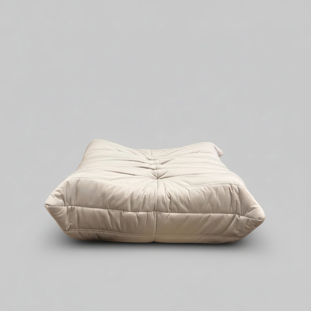 White cushion on a wooden floor with a black and white patterned rug and a painting of a cityscape in the background.