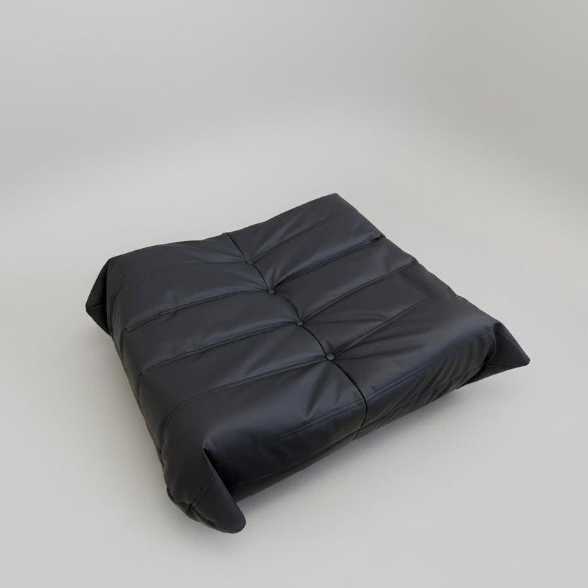 Black cushion on a wooden floor with a white wall and electrical outlet in the background.