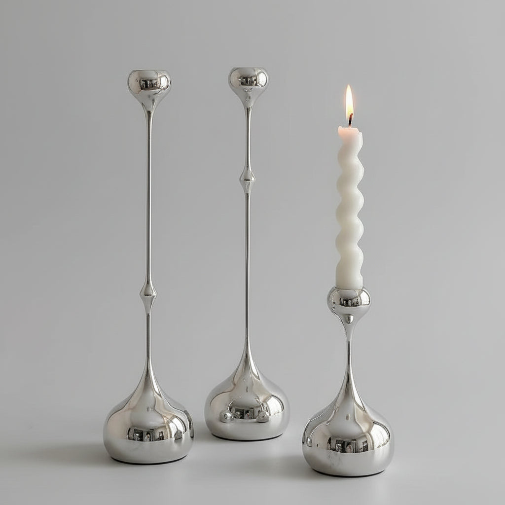 Three silver candle holders on a table with a white candle.