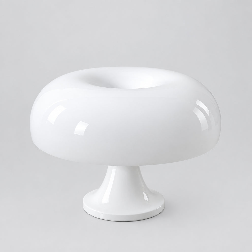 A glossy white mushroom-shaped table lamp with a wide rounded cap and a short pedestal base, shown on a light wood surface against a plain beige wall.