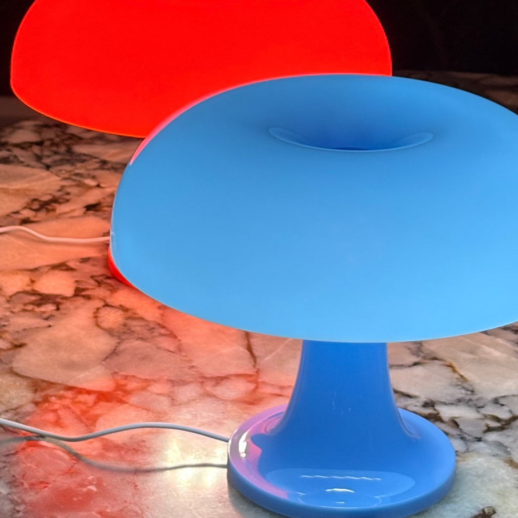 Two colorful table lamps, one red and one blue, on a marble surface with a dark background.