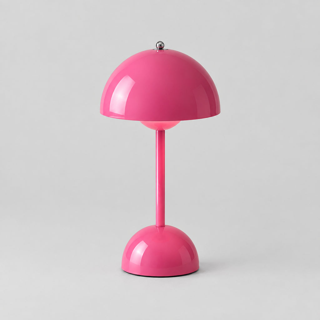 A bright pink mushroom-shaped table lamp with a glowing warm light, styled next to a book and a small teacup on a light gray background.