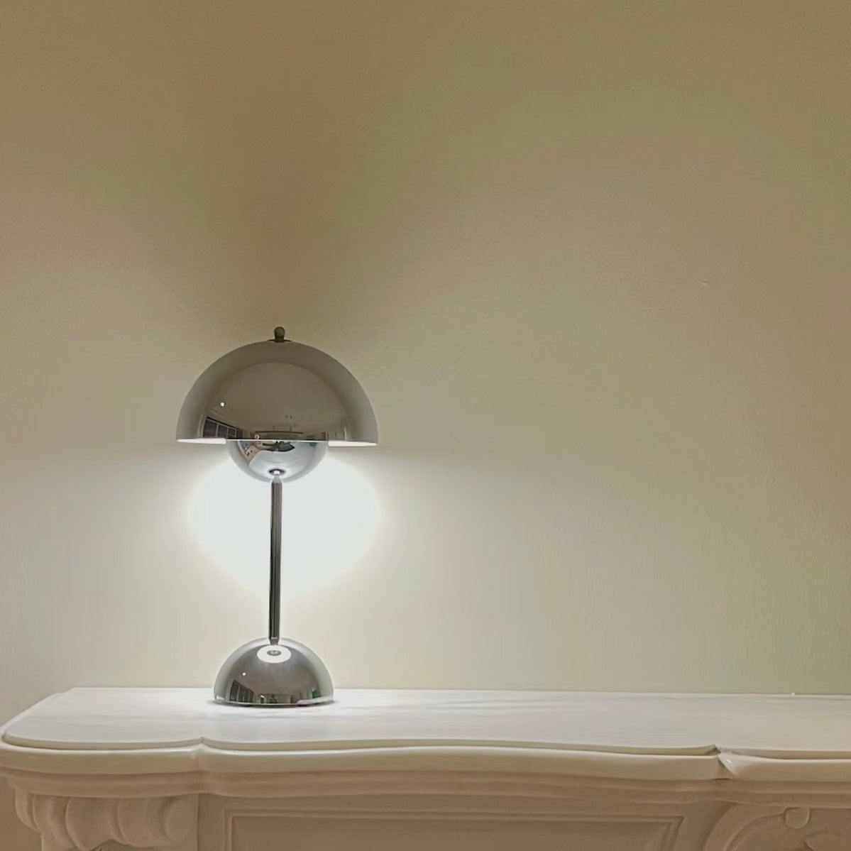 Modern silver lamp on a white surface with a plain wall background