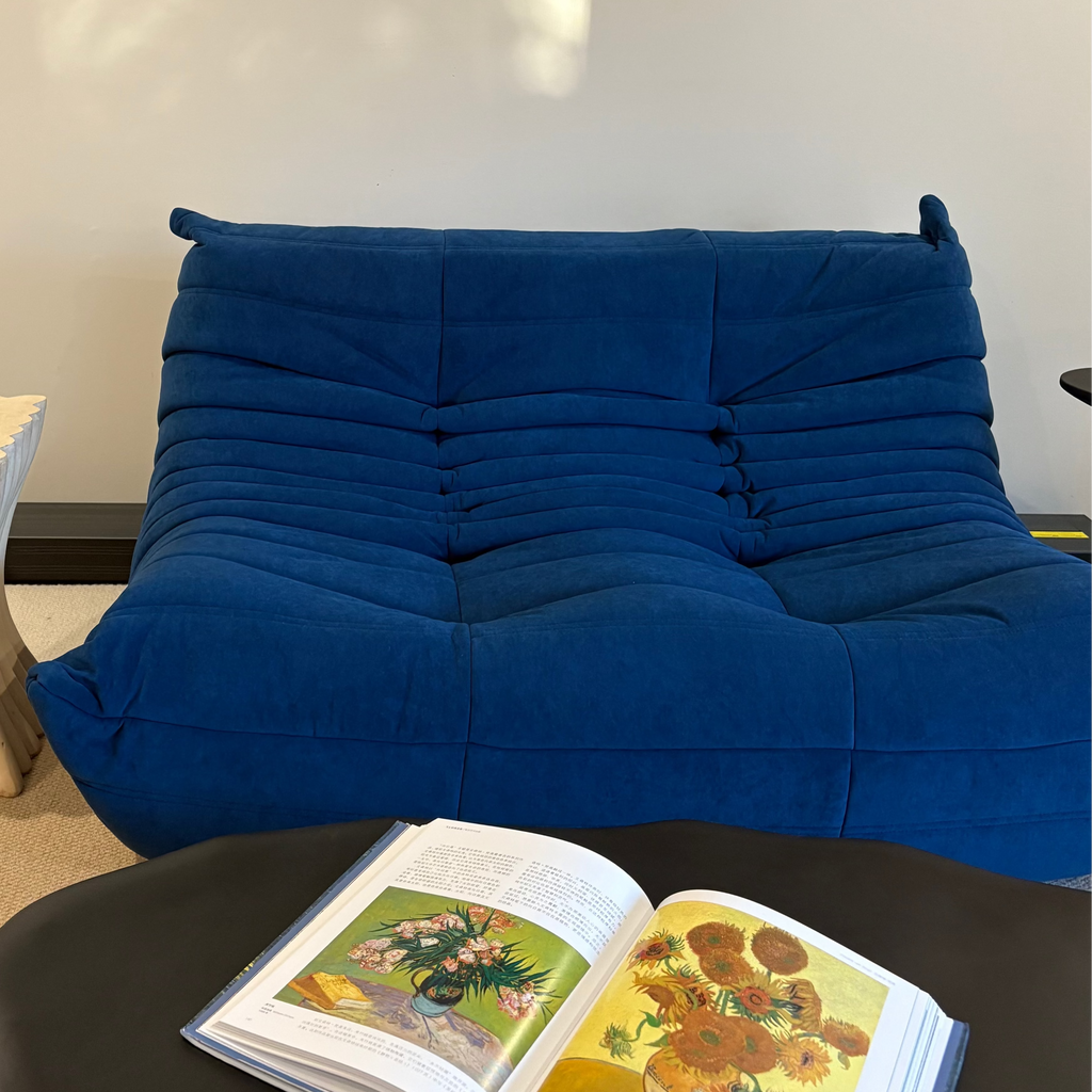 Blue sofa with an open book featuring Van Gogh's 'Sunflowers' on a black table, against a white wall with a painting.