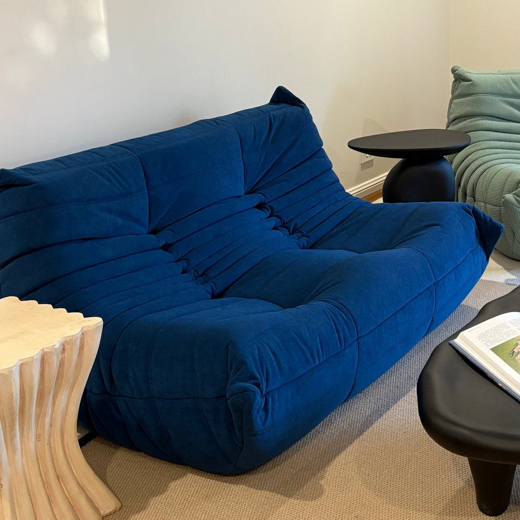 Modern living room with blue sofa, green chair, and round black coffee table.