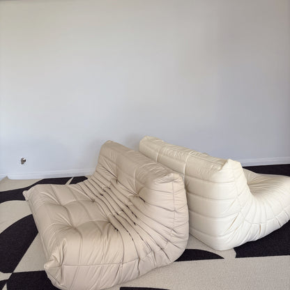Beige modern sofa on a black and white patterned rug against a white wall