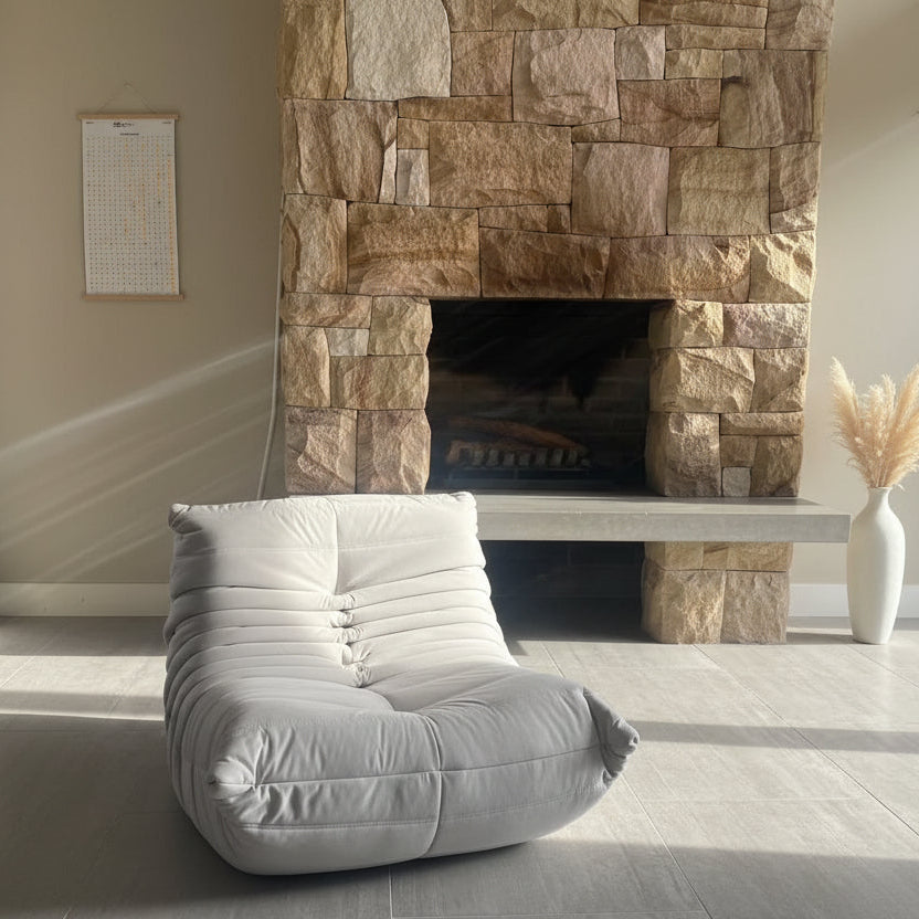 White lounge chair in front of a stone fireplace in a room with light gray flooring.