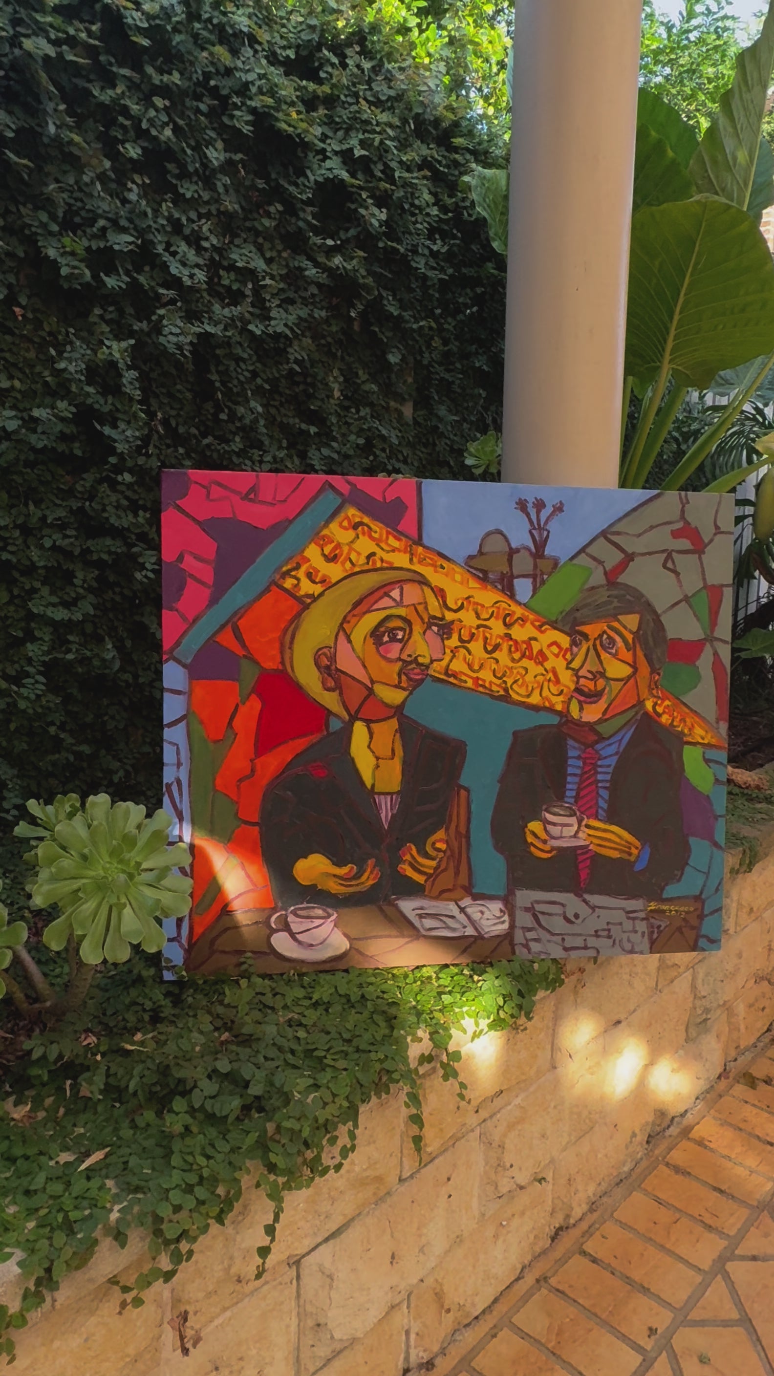 A bold and vibrant cubist painting featuring two figures engaged in conversation over coffee at a café. The artwork is rich with geometric shapes, expressive faces, and a striking colour palette of reds, yellows, and blues, evoking a lively and intellectual atmosphere.